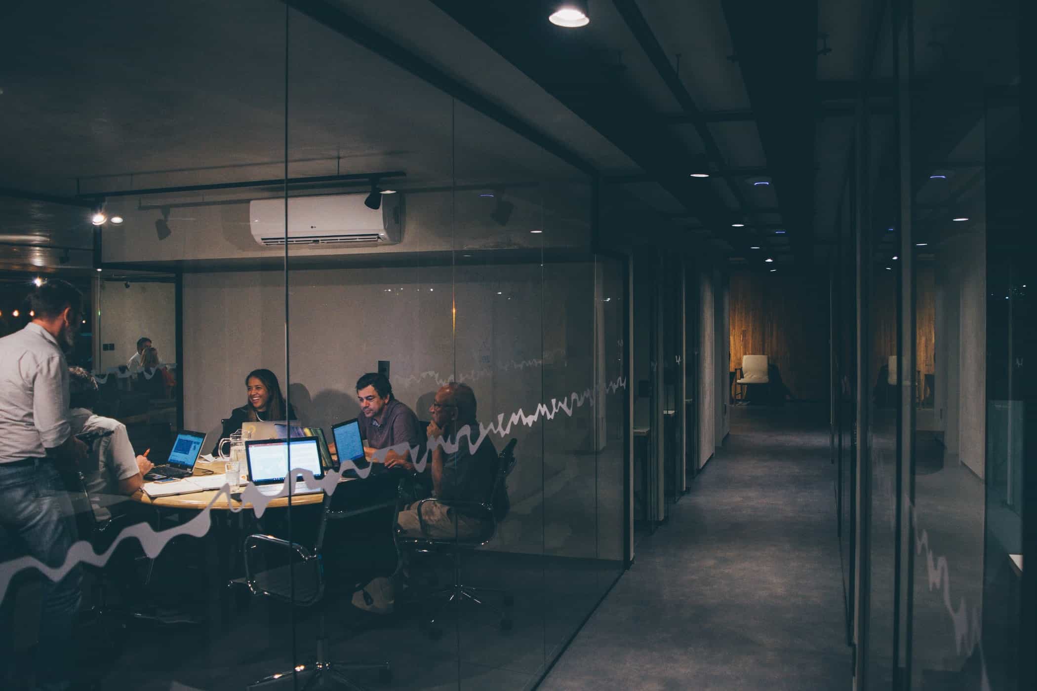 Colleagues gathered around laptops in a glass meeting room.